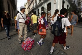 Dos estudiantes de la enseñanza primaria caminan próximo a un grupo de turistas extranjeros en una céntrica Plaza del centro histórico de La Habana Vieja, La Habana, Cuba.